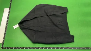 Full back view of a black crewneck knit sweater on the same green warehouse inspection mat with rulers