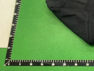 Framed view of the green inspection mat corner and edge rulers beside the garment
