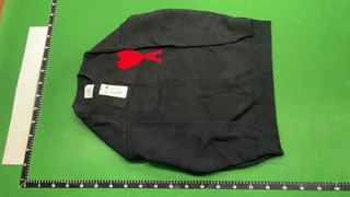 Full front view of a black crewneck knit sweater with a red chest design on a green warehouse inspection mat with rulers